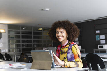 Lächelnder Universitätsstudent, der in der Bibliothek ein digitales Tablet benutzt - PNAF01813