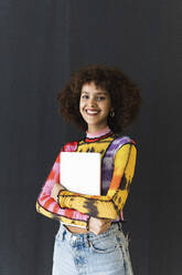 Female student standing with book in front of black wall - PNAF01822