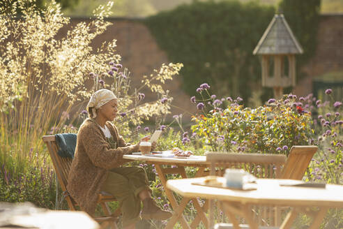 Woman with digital tablet and coffee at sunny garden cafe table - CAIF30522