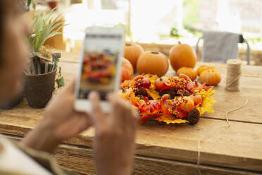 Florist mit Fotohandy beim Fotografieren der Herbstauslage im Geschäft - CAIF30534