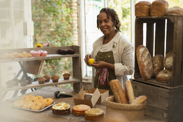 Portrait female baker arranging display in shop - CAIF30536