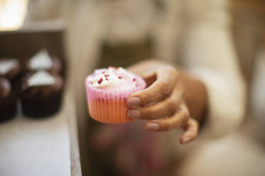 Close up female baker holding cupcake in pink liner - CAIF30539