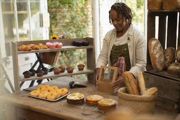 Female baker boxing pastries in shop - CAIF30544