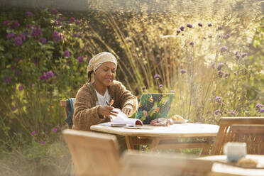 Frau arbeitet am Laptop am Tisch eines idyllischen Gartencafés - CAIF30549