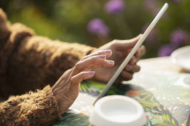Nahaufnahme einer Frau, die ein digitales Tablet am Terrassentisch benutzt - CAIF30552