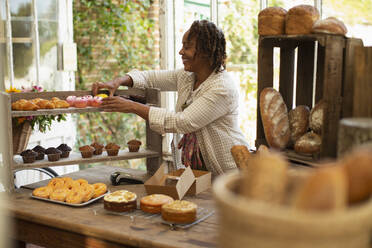 Female baker arranging pastry display in shop - CAIF30567