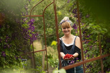Porträt stolze Frau erntet frische rote Johannisbeeren im Garten - CAIF30586