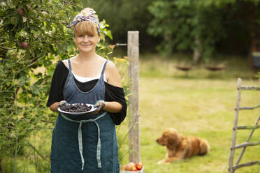 Portrait proud woman with blackberries in summer garden - CAIF30610