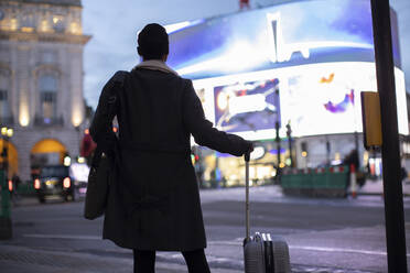 Frau mit Koffer an einer nächtlichen Straßenecke, London, UK - CAIF30613