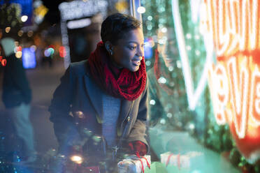 Junge Frau mit Weihnachtstüten vor einem nächtlichen Neon-Schaufenster - CAIF30618