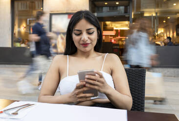 Junge Frau benutzt ihr Smartphone, während sie in einem Café am Tisch sitzt - JCCMF02660