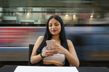 Young woman using mobile phone while sitting at table in cafe during dusk - JCCMF02662