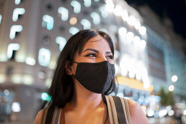 Junge Frau mit Gesichtsschutzmaske, die in der Dämmerung wegschaut - JCCMF02665