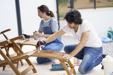 Mid adult boyfriend and girlfriend painting deck chair in new house - JSMF02258