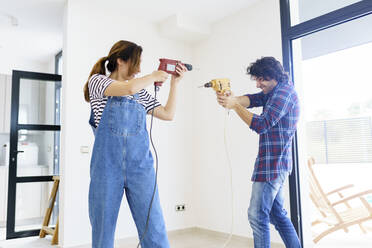 Mid adult couple playing with drill machine in new home - JSMF02265