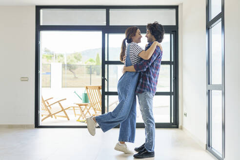 Mid adult couple embracing while relocating in new home - JSMF02273