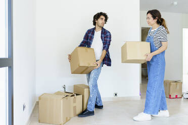 Young man and woman carrying cardboard boxes in new home - JSMF02275