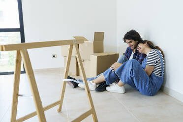 Happy girlfriend leaning on boyfriend by boxes in new home - JSMF02276