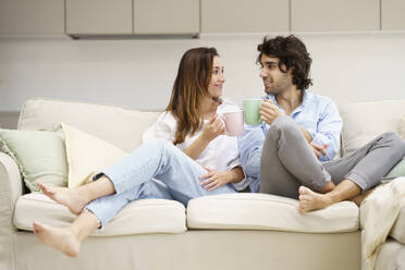 Smiling couple having coffee while sitting on sofa at new home - JSMF02290