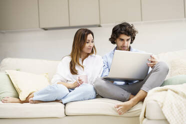 Mid adult man using laptop while girlfriend sitting besides on sofa in new home - JSMF02291