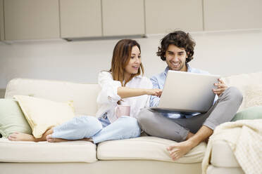 Ehepaar unterhält sich auf dem Sofa in der neuen Wohnung mit einem Laptop - JSMF02292