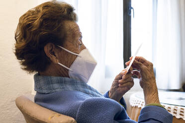 Senior woman in protective face mask looking at photograph - JCCMF02668