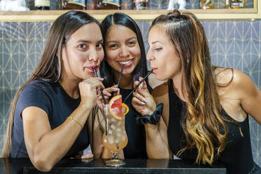 Lächelnde Freundinnen trinken einen Cocktail an einer Bar - DLTSF01906