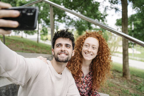 Lächelndes junges Paar nimmt Selfie durch Handy in öffentlichen Park - JCZF00762