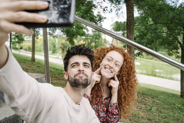 Junges Paar macht niedliche Gesichter beim Selfie machen im öffentlichen Park - JCZF00763