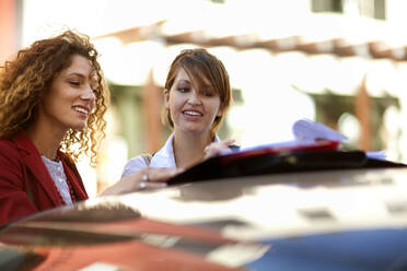 Geschäftsfrauen erledigen Papierkram, während sie eine Akte im Auto führen - AJOF01433