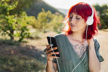 Hipster woman with red hair using smart phone during sunny day - MRRF01165