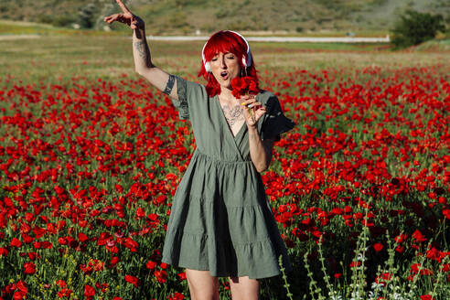 Junge Frau hält einen Blumenstrauß und singt auf einem Mohnfeld - MRRF01181