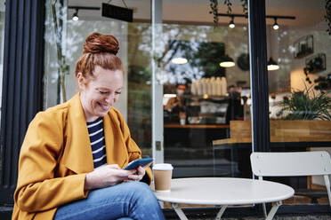 Lächelnde Frau, die ein Smartphone benutzt, während sie in einem Café sitzt - ASGF00354