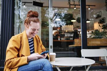 Smiling woman using smart phone while sitting at cafe - ASGF00354