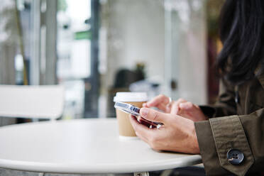 Frau benutzt Smartphone in einem Straßencafé - ASGF00356