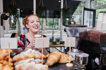 Lächelnde Frau mit Einweg-Kaffeebecher an der Theke eines Cafés - ASGF00359
