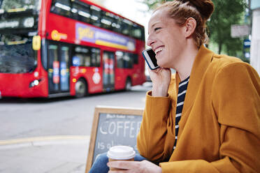 Smiling woman talking on mobile phone at sidewalk cafe - ASGF00366