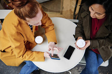 Frau zeigt einer Freundin ihr Smartphone, während sie im Cafe sitzt - ASGF00368