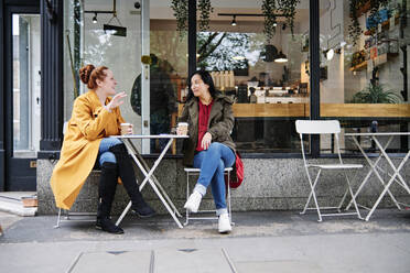 Frau gestikuliert im Gespräch mit einer Freundin vor einem Café - ASGF00369