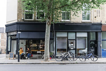 Female friends talking while sitting at sidewalk cafe - ASGF00370