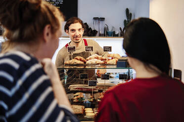 Männlicher Besitzer schaut Frauen an, die am Tresen eines Cafés stehen - ASGF00381