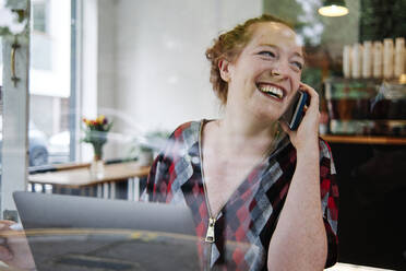 Glückliche Frau im mittleren Erwachsenenalter, die wegschaut, während sie in einem Café mit einem Mobiltelefon spricht - ASGF00396