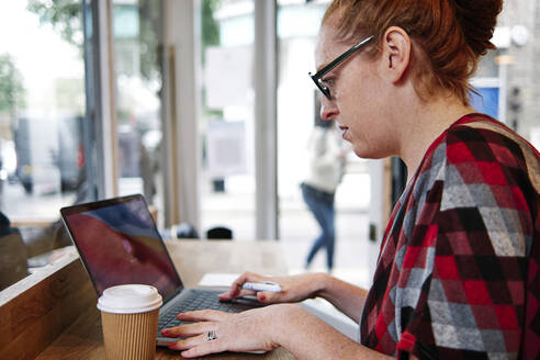 Frau mit Brille benutzt Laptop in einem Cafe - ASGF00404