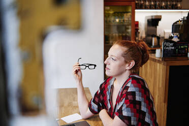 Woman with eyeglasses contemplating while sitting at cafe - ASGF00406