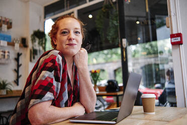 Mittlere erwachsene Frau lehnt sich in einem Café vor einem Laptop auf den Tisch - ASGF00410