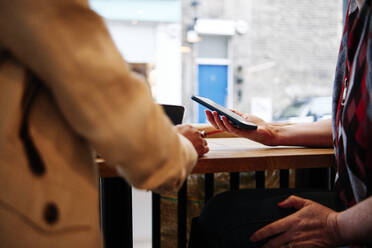 Women holding smart phone sitting at coffee table - ASGF00420