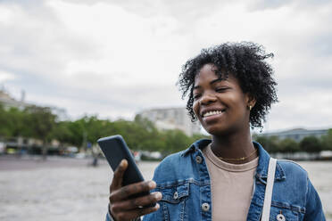 Lächelnde Frau mit Mobiltelefon in der Stadt - XLGF01993