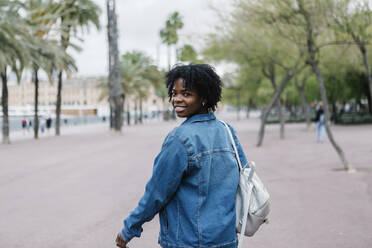 Smiling woman with backpack looking back over shoulder - XLGF01998