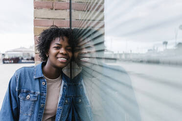 Smiling Afro woman leaning on glass window - XLGF02005