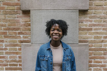 Cheerful woman wearing denim jacket standing in front of wall - XLGF02008